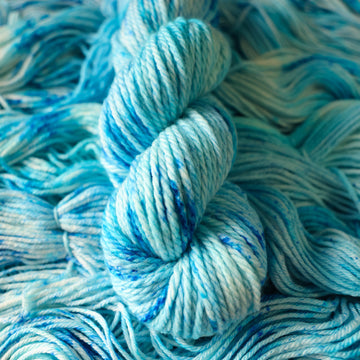 A Bulky skein of yarn colored bright and frosty blue with cobalt speckles. The skein is sitting on the unwrapped yarn.