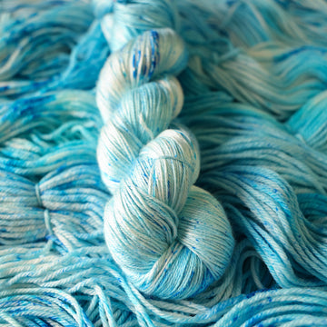 A silk skein of yarn colored bright and frosty blue with cobalt speckles. The skein is sitting on the unwrapped yarn.
