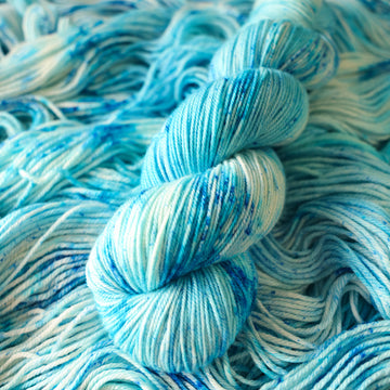 A sport skein of yarn colored bright and frosty blue with cobalt speckles. The skein is sitting on the unwrapped yarn.