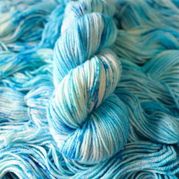 A worsted skein of yarn colored bright and frosty blue with cobalt speckles. The skein is sitting on the unwrapped yarn.