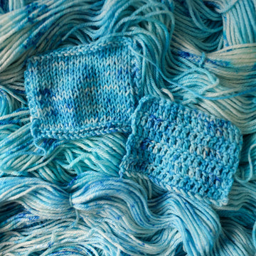 two knit and crochet swatches of yarn colored bright and frosty blue with cobalt speckles. The skein is sitting on the unwrapped yarn.