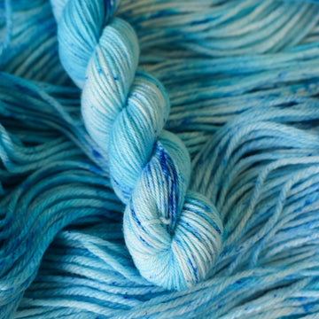 A fingering mini skein of yarn colored bright and frosty blue with cobalt speckles. The skein is sitting on the unwrapped yarn.