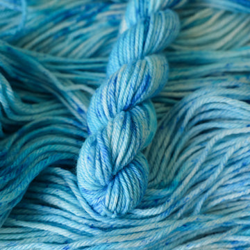 A DK Mini skein of yarn colored bright and frosty blue with cobalt speckles. The skein is sitting on the unwrapped yarn.