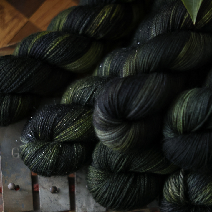 several skeins of dark green and black variegated yarn stacked together on a wooden surface