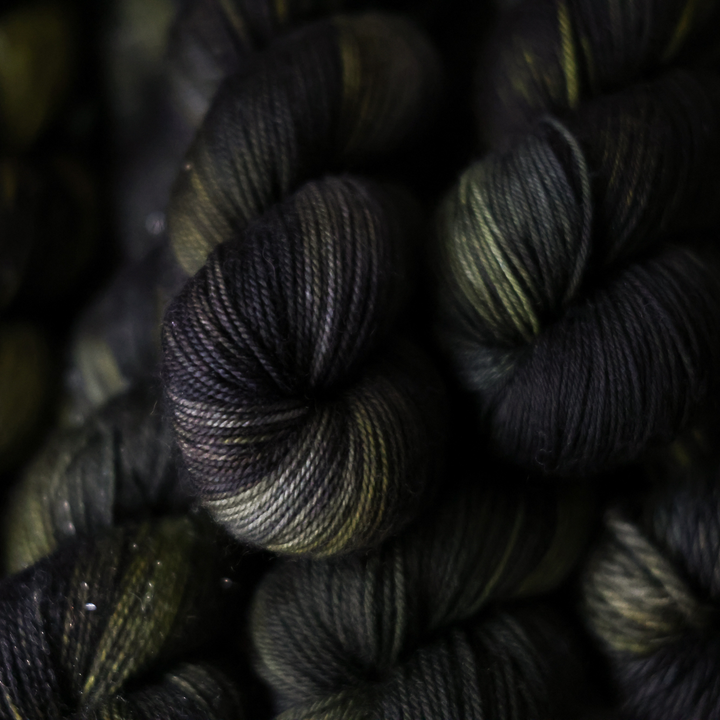 close-up of several skeins of dark-colored yarn, primarily in shades of black, green, and brown