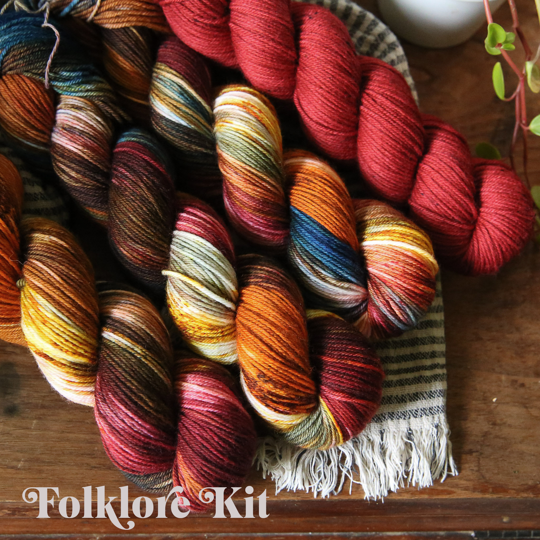 four skeins of multicolored and red yarn rest on a striped woven cloth on a wooden surface