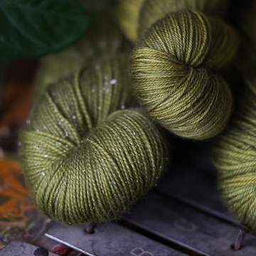 close-up of skeins of soft, olive green yarn with a subtle shimmer, resting on a rustic surface