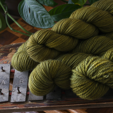 three skeins of olive green yarn rest on a wooden tray beside a vintage metal hook