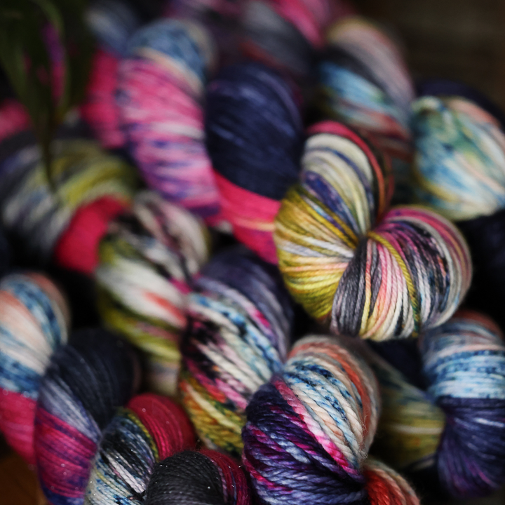several skeins of yarn in vibrant colors, including shades of blue, pink, yellow, purple, and white, are artfully arranged together in a close-up view