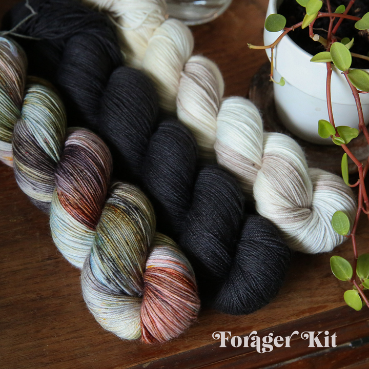 yarn skeins arranged on a wooden surface, in black, cream, and multi-colored