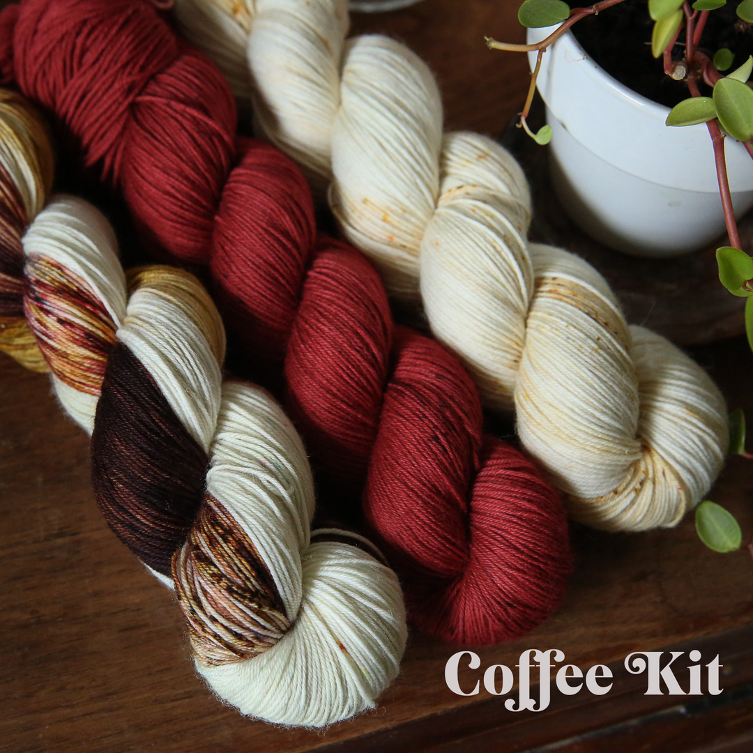 three skeins of yarn in cream, red, and a cream-brown mix on a wooden surface