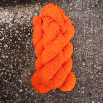 A couple of vibrant orange Sport yarn skeins on top of gravel.