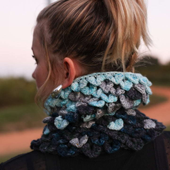 Photo of women from the back wearing Voidebane cowl, dragon scale crochet with icy blue, grey, dark blue and black colors.